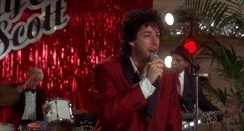 Movie still from “The Wedding Singer” (1998), directed by Frank Coraci – A man in a red jacket is singing into a microphone; Medium shot, Over the shoulder angle