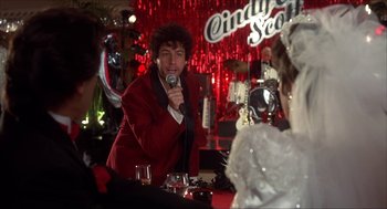 Movie still from “The Wedding Singer” (1998), directed by Frank Coraci – A man in a red jacket is holding a microphone; Medium shot, Over the shoulder angle