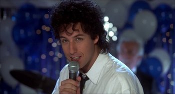 Movie still from “The Wedding Singer” (1998), directed by Frank Coraci – A man with curly hair is holding a microphone; Close Up shot, Over the shoulder angle