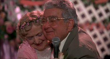 Movie still from “The Wedding Singer” (1998), directed by Frank Coraci – An older man holding a microphone next to an older woman; Close Up shot, High angle