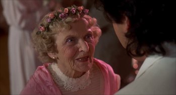 Movie still from “The Wedding Singer” (1998), directed by Frank Coraci – An older woman wearing a pink dress with flowers in her hair; Close Up shot, Over the shoulder angle