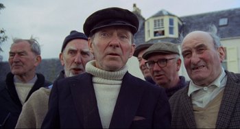 Movie still from “The Wicker Man” (1973), directed by Robin Hardy – An older man wearing a sweater and a hat; Medium shot, Low angle