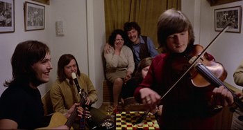 Movie still from “The Wicker Man” (1973), directed by Robin Hardy – A group of people sitting in a living room playing instruments; Medium shot, High angle