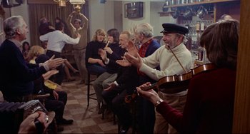 Movie still from “The Wicker Man” (1973), directed by Robin Hardy – A group of people sitting in a living room playing instruments; Wide shot, High angle