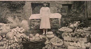 Movie still from “The Wicker Man” (1973), directed by Robin Hardy – An old black and white photo of a woman standing in front of a bunch of vegetables; Wide shot, Overhead angle