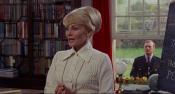 Movie still from “The Wicker Man” (1973), directed by Robin Hardy – A woman in a white shirt is standing in front of a window; Medium shot, Over the shoulder angle