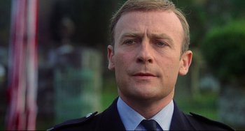 Movie still from “The Wicker Man” (1973), directed by Robin Hardy – A person wearing a suit and tie; Close Up shot, Low angle