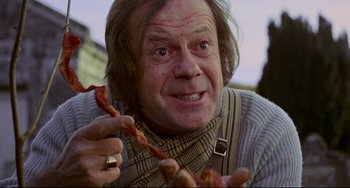 Movie still from “The Wicker Man” (1973), directed by Robin Hardy – An older man holding a bunch of food in his hands; Close Up shot, Low angle