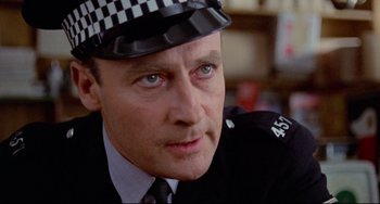 Movie still from “The Wicker Man” (1973), directed by Robin Hardy – A man in a police officer's uniform with a checkered hat; Close Up shot, Low angle