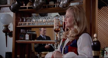 Movie still from “The Wicker Man” (1973), directed by Robin Hardy – A woman is sitting at a bar with a man in the background; Medium shot, Over the shoulder angle
