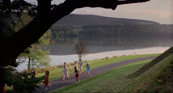 Movie still from “The Wicker Man” (1973), directed by Robin Hardy – A group of people walking down a road next to a body of water; Extreme Wide shot, High angle