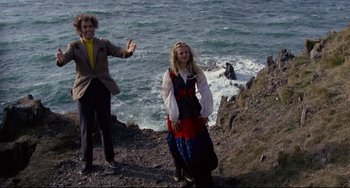 Movie still from “The Wicker Man” (1973), directed by Robin Hardy – A man and a woman standing next to a body of water; Wide shot, Low angle