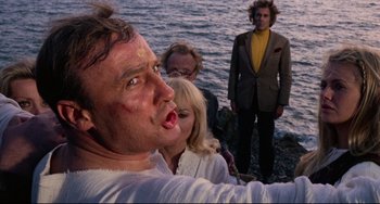 Movie still from “The Wicker Man” (1973), directed by Robin Hardy – A group of people standing next to a body of water; Medium shot, Low angle