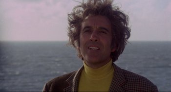 Movie still from “The Wicker Man” (1973), directed by Robin Hardy – A man in a yellow shirt and a brown jacket is by the ocean; Close Up shot, Low angle