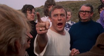 Movie still from “The Wicker Man” (1973), directed by Robin Hardy – A group of people standing in a field with one man pointing at the camera; Medium shot, Low angle