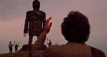 Movie still from “The Wicker Man” (1973), directed by Robin Hardy – A man is holding a torch in front of a giant statue; Wide shot, Low angle