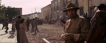 Movie still from “The Wild Bunch” (1969), directed by Sam Peckinpah – A man wearing a hat and a uniform standing in the middle of a dirt field; Medium shot, Over the shoulder angle
