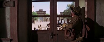 Movie still from “The Wild Bunch” (1969), directed by Sam Peckinpah – A man in a cowboy hat is looking out of a door; Wide shot, Low angle