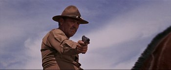 Movie still from “The Wild Bunch” (1969), directed by Sam Peckinpah – A man holding a gun while wearing a hat; Medium shot, Low angle