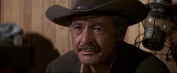 Movie still from “The Wild Bunch” (1969), directed by Sam Peckinpah – An older man wearing a cowboy hat and looking at the camera; Close Up shot, Over the shoulder angle