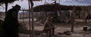 Movie still from “The Wild Bunch” (1969), directed by Sam Peckinpah – A man sitting on the ground in front of a hut; Wide shot, Low angle