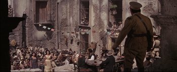 Movie still from “The Wild Bunch” (1969), directed by Sam Peckinpah – A group of people sitting at tables outside of a brick building; Wide shot, High angle