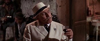 Movie still from “The Wild Bunch” (1969), directed by Sam Peckinpah – An older man in a white suit and a white hat is holding a glass of red wine; Close Up shot, High angle