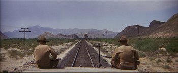 Movie still from “The Wild Bunch” (1969), directed by Sam Peckinpah – Two men are sitting on the side of a train track; Wide shot, Low angle