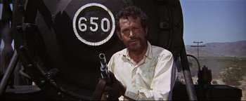 Movie still from “The Wild Bunch” (1969), directed by Sam Peckinpah – A man holding a gun in front of a train; Medium shot, Low angle