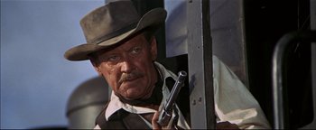 Movie still from “The Wild Bunch” (1969), directed by Sam Peckinpah – A man holding a gun while standing next to a pole; Close Up shot, Low angle