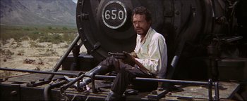 Movie still from “The Wild Bunch” (1969), directed by Sam Peckinpah – A man sitting on top of a train holding a gun; Medium shot, Low angle