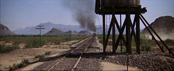 Movie still from “The Wild Bunch” (1969), directed by Sam Peckinpah – A train traveling down train tracks next to mountains; Extreme Wide shot, High angle