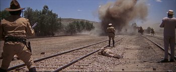 Movie still from “The Wild Bunch” (1969), directed by Sam Peckinpah – A man standing next to train tracks next to a body; Extreme Wide shot, Low angle