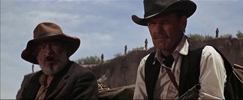 Movie still from “The Wild Bunch” (1969), directed by Sam Peckinpah – Two men sitting next to each other on top of a hill; Close Up shot, Low angle