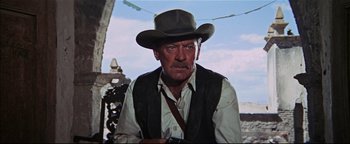 Movie still from “The Wild Bunch” (1969), directed by Sam Peckinpah – An older man wearing a cowboy hat while holding a camera; Medium shot, Low angle