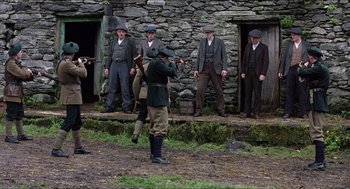 Movie still from “The Wind that Shakes the Barley” (2006), directed by Ken Loach – A group of men standing in front of a stone building; Wide shot, Low angle