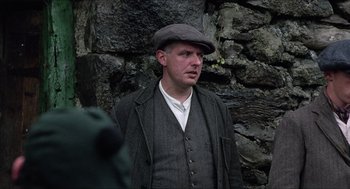 Movie still from “The Wind that Shakes the Barley” (2006), directed by Ken Loach – A man wearing a hat standing in front of a stone wall; Close Up shot, Over the shoulder angle