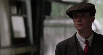 Movie still from “The Wind that Shakes the Barley” (2006), directed by Ken Loach – A man in a suit and a hat is standing in front of a window; Close Up shot, Low angle