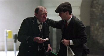 Movie still from “The Wind that Shakes the Barley” (2006), directed by Ken Loach – Two men in suits and hats are talking to each other; Medium shot, Over the shoulder angle
