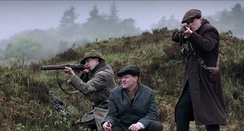 Movie still from “The Wind that Shakes the Barley” (2006), directed by Ken Loach – A group of people in a field with a gun; Medium shot, Low angle