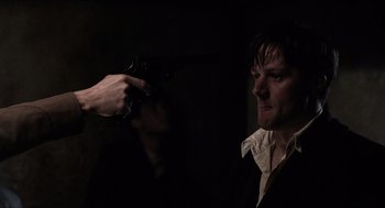 Movie still from “The Wind that Shakes the Barley” (2006), directed by Ken Loach – A man holding a gun in front of another man in a dark room; Close Up shot, Over the shoulder angle