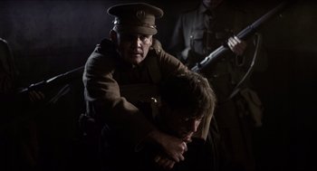 Movie still from “The Wind that Shakes the Barley” (2006), directed by Ken Loach – A man in a military uniform holding another man in his arms; Medium shot, Over the shoulder angle