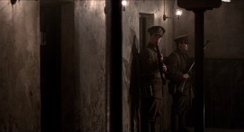 Movie still from “The Wind that Shakes the Barley” (2006), directed by Ken Loach – Two men dressed in uniforms are standing in a hallway; Wide shot, Low angle