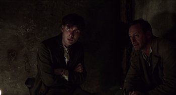 Movie still from “The Wind that Shakes the Barley” (2006), directed by Ken Loach – A man sitting next to another man in a dark room; Medium shot, Over the shoulder angle