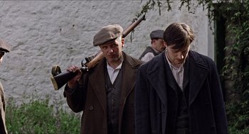 Movie still from “The Wind that Shakes the Barley” (2006), directed by Ken Loach – A group of men walking down a street holding guns; Medium shot, Over the shoulder angle