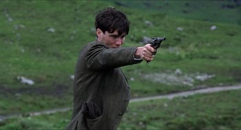 Movie still from “The Wind that Shakes the Barley” (2006), directed by Ken Loach – A man holding a gun while standing in a field; Medium shot, Low angle
