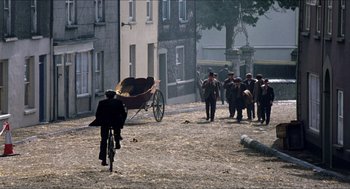 Movie still from “The Wind that Shakes the Barley” (2006), directed by Ken Loach – A group of people standing on a dirt road near a horse drawn carriage; Extreme Wide shot, High angle
