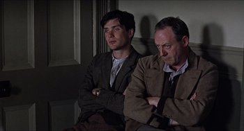 Movie still from “The Wind that Shakes the Barley” (2006), directed by Ken Loach – Two men sitting next to each other in front of a wall; Medium shot, Low angle