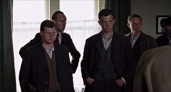 Movie still from “The Wind that Shakes the Barley” (2006), directed by Ken Loach – A group of men standing next to each other in front of a window; Medium shot, Low angle