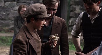 Movie still from “The Wind that Shakes the Barley” (2006), directed by Ken Loach – Two men in brown jackets and hats looking at a rope; Medium shot, Over the shoulder angle